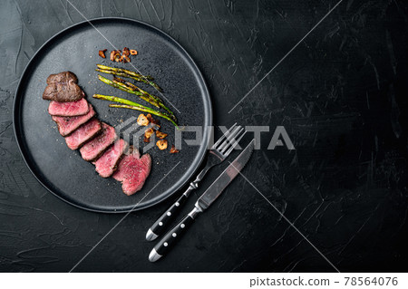 Juicy steak medium rare beef Filet Mignon or Eye Fillet, with onion and asparagus, on plate, with meat knife and fork, on black stone background, top view flat lay, with copy space for text 78564076