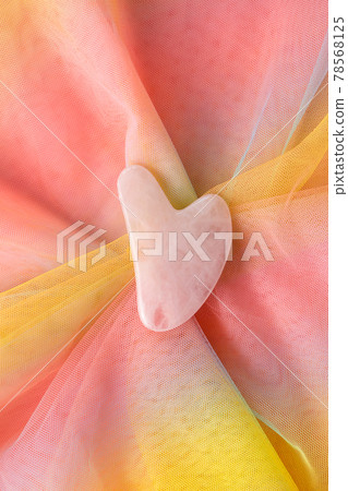 Gua sha on colorful rainbow organza fabric, top view. Trendy skincare facial massager tool guasha Gua sha on colorful rainbow organza fabric, top view. Trendy skincare facial massager tool guasha 78568125