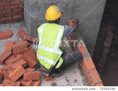 JOHOR, MALAYSIA -NOVEMBER 25, 2016: Bricklayer lay clay bricks block to form building walls at the construction site. JOHOR, MALAYSIA -NOVEMBER 25, 2016: Bricklayer lay clay bricks block to form building walls at the construction site. 78568596