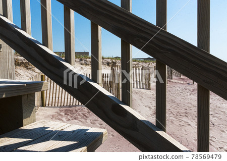 Looking through the railing of a staircase on the beach at fencing protecting the dunes Looking through the railing of a staircase on the beach at fencing protecting the dunes 78569479