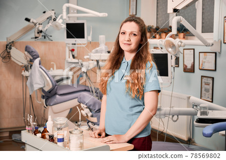 Charming female dentist standing in stomatology cabinet. Charming female dentist standing in stomatology cabinet. 78569802