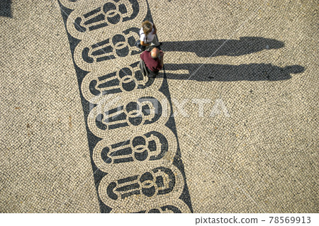 Long shadows of people on a square with pattern of paving stones in Lisbon photographed from above 78569913