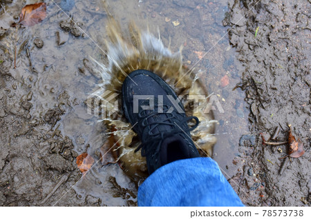 Water splash from shoes. Men's feet in hiking shoes steps into a puddle.  78573738