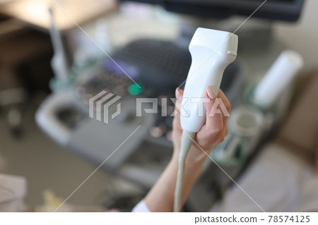 Doctor holding ultrasound probe in his hand in clinic closeup 78574125