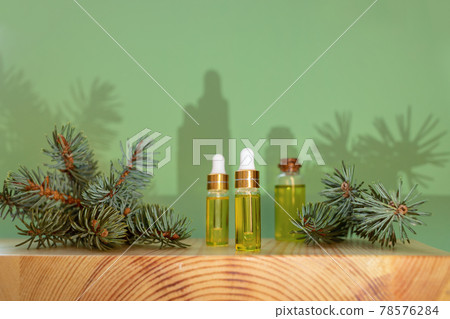 Creative Christmas aromatherapy and spa composition with trendy shadows. Essential coniferous spruce oil in small glass bottles and green twigs on wooden boxwood stand on light green backdrop. Creative Christmas aromatherapy and spa composition with trendy shadows. Essential coniferous spruce oil in small glass bottles and green twigs on wooden boxwood stand on light green backdrop. 78576284