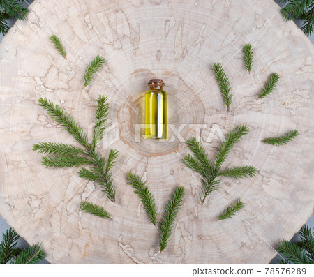 Small glass bottle with coniferous spa aromatic essential spruce oil with green twigs around it in center of wooden saw cut. Christmas aromatherapy and spa concept. View from above. Small glass bottle with coniferous spa aromatic essential spruce oil with green twigs around it in center of wooden saw cut. Christmas aromatherapy and spa concept. View from above. 78576289