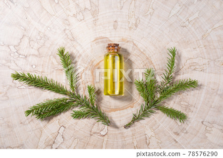 Small glass bottle with coniferous spa aromatic essential spruce oil and two small branches on wooden saw cut. Minimal Christmas aromatherapy and spa concept. View from above. 78576290