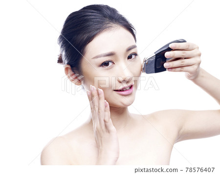 young asian woman using a face spa instrument, isolated on white 78576407