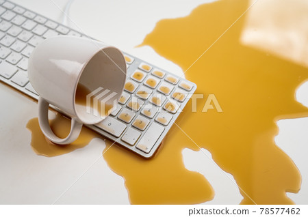 Spilled cup of black coffee on computer keyboard on white table. Spilled cup of black coffee on computer keyboard on white table. 78577462