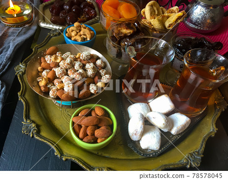 A table with Turkish tea with lale, oriental sweets, rahad delight, a mix of various nuts using copper dishes and bright fabrics. 78578045