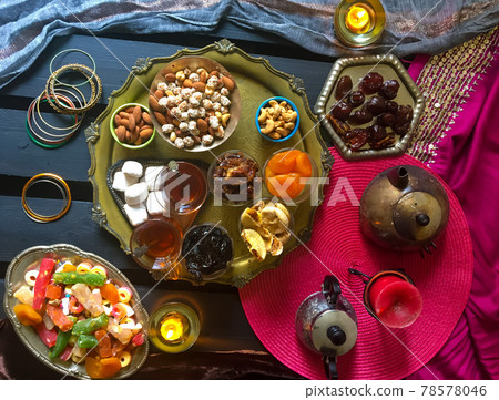 A table with Turkish tea with lale, oriental sweets, rahad delight, a mix of various nuts using copper dishes and bright fabrics. 78578046