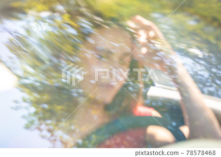 Motion blured image of happy young woman driving a car on a summer road trip travel vacations. Shot trough windshield. Motion blured image of happy young woman driving a car on a summer road trip travel vacations. Shot trough windshield. 78578468