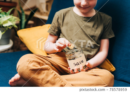 Close up of Little child kid boy hands grabbing and putting stack coins in to glass jar with save label. Donation, saving money, charity, family finance plan concept 78578959