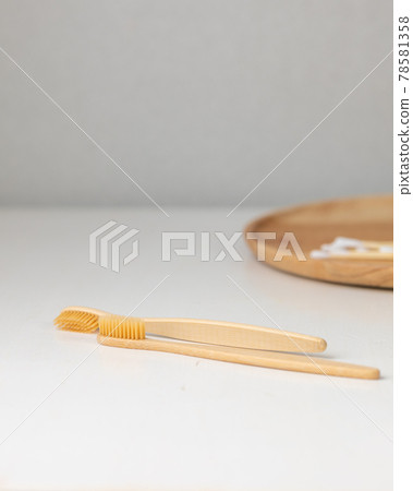 daily human hygiene, cotton swabs and cotton pads, a woman's hand holding bamboo toothbrushes on a light background in a glass or against the background of a wooden tray daily human hygiene, cotton swabs and cotton pads, a woman's hand holding bamboo toothbrushes on a light background in a glass or against the background of a wooden tray 78581358