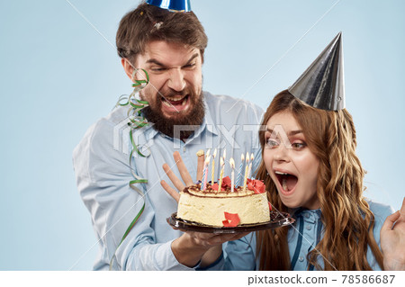 Birthday man woman in party hats on a blue background and cake with candles Birthday man woman in party hats on a blue background and cake with candles 78586687