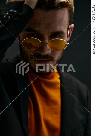 a brutal guy with glasses and a black jacket orange sweater dark background  78587132