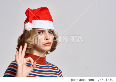 Happy woman in a Christmas cap and a striped sweater gestures with her hands for the New Year holidays 78591830