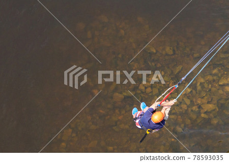 Rope jumping from high altitude of bridge. Bungee jumping from pedestrian bridge over beautiful river 78593035
