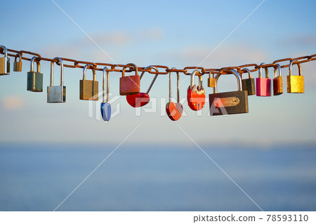 Various and heart colorful shaped love padlocks on a chain on a beautiful blue sky and sea background. Diverse locks as a symbol of togetherness and bonding. Various and heart colorful shaped love padlocks on a chain on a beautiful blue sky and sea background. Diverse locks as a symbol of togetherness and bonding. 78593110