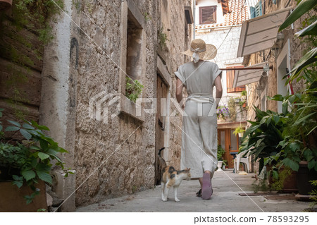 Rear view of beautiful blonde young female traveler wearing straw sun hat sightseeing and enjoying summer vacation in an old traditional costal town at Adriatic cost, Croatia Rear view of beautiful blonde young female traveler wearing straw sun hat sightseeing and enjoying summer vacation in an old traditional costal town at Adriatic cost, Croatia 78593295