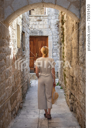 Rear view of beautiful blonde young female traveler wearing straw sun hat sightseeing and enjoying summer vacation in an old traditional costal town at Adriatic cost, Croatia 78593430