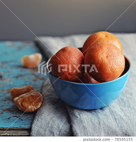 fresh delicious tangerines in blue bowl side view on gray towel on blue rustic background closeup. Selective focus 78595155