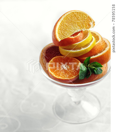 fresh citrus oranges and lemons sliced in glass vase with mint side view on white background closeup. Selective focus 78595158