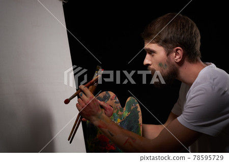 A man with a palette in his hands brush easel art Creative approach hobby dark background A man with a palette in his hands brush easel art Creative approach hobby dark background 78595729