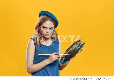 Woman with palette in blue hands takes paintbrush hobby artwork yellow background Woman with palette in blue hands takes paintbrush hobby artwork yellow background 78595772