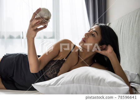Woman in sexy pajama hold skull on bed. 78596641