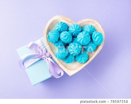 Blue pastel gift box with purple ribbon and heart shaped dish of sweet meringues 78597358