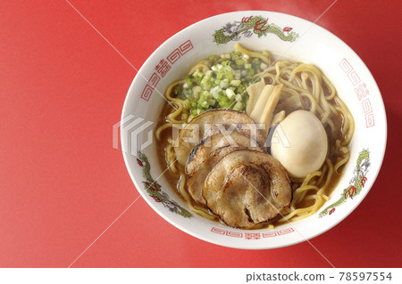 A bird's-eye view of hot pork bone soy sauce ramen with roasted char siu, taste balls, menma and all-purpose green onions on a red background 78597554