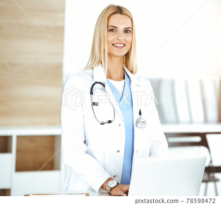 Woman-doctor controls medication history records and exam results while using laptop computer in sunny hospital. Medicine and healthcare concept 78598472