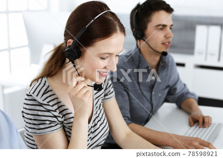 Casual dressed young woman using headset and computer while talking with customers online. Group of operators at work. Call center, business concept Casual dressed young woman using headset and computer while talking with customers online. Group of operators at work. Call center, business concept 78598921