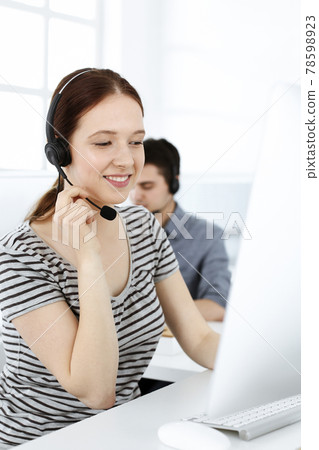 Casual dressed young woman using headset and computer while talking with customers online. Group of operators at work. Call center, business concept 78598923