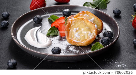 Tasty baked pancakes with berries and mint with powdered sugar and topping on a gray plate Tasty baked pancakes with berries and mint with powdered sugar and topping on a gray plate 78602026