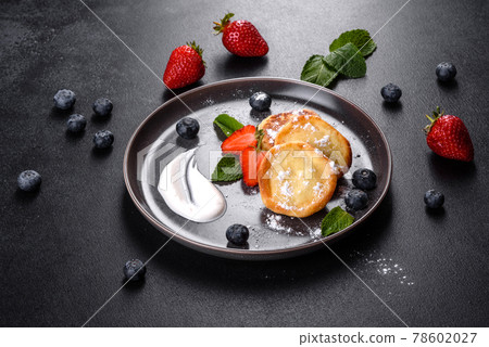 Tasty baked pancakes with berries and mint with powdered sugar and topping on a gray plate Tasty baked pancakes with berries and mint with powdered sugar and topping on a gray plate 78602027
