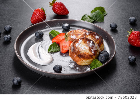 Tasty baked pancakes with berries and mint with powdered sugar and topping on a gray plate Tasty baked pancakes with berries and mint with powdered sugar and topping on a gray plate 78602028