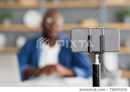 Mature black man blogger broadcasting from home, talking to phone camera, selective focus on smartphone 78605038