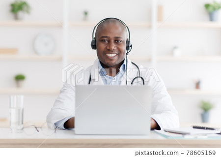 Blog and answer patient questions. Happy african american doctor with headphones and laptop computer at workplace Blog and answer patient questions. Happy african american doctor with headphones and laptop computer at workplace 78605169