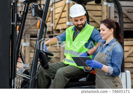 Millennial bearded man in helmet in forklift truck, discussing order with smiling woman 78605171