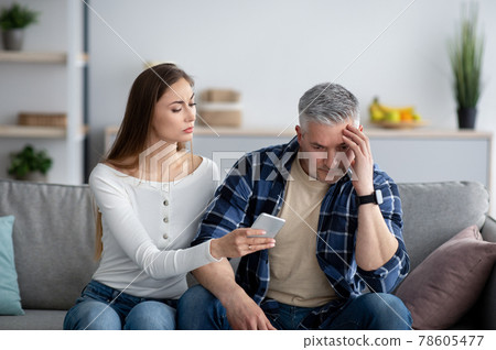 Mature woman confronting her husband about correspondence with his lover on smartphone 78605477