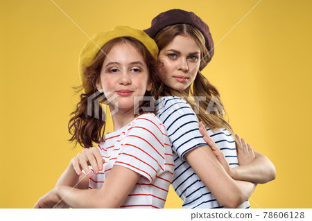 Cheerful sisters in hats striped T-shirts joy lifestyle yellow background family 78606128
