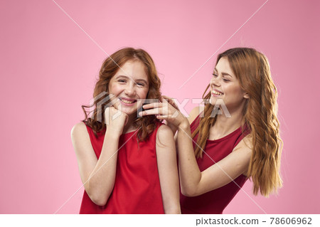 Cheerful mom and daughter wearing red dresses are standing next to joy family on pink background 78606962
