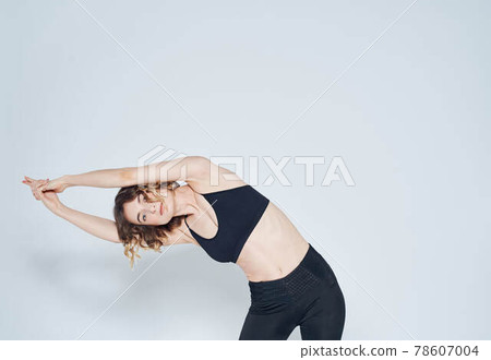 A woman in leggings has joined her hands above her head and is doing the exercises, bends to the side A woman in leggings has joined her hands above her head and is doing the exercises, bends to the side 78607004