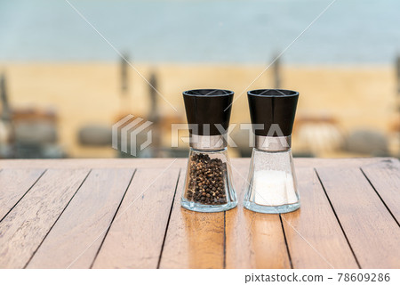 Salt and peppercorn grinder bottles on cafe table near beach. 78609286