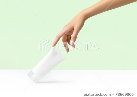 Womans hand holding white tube on pastel green background 78609806