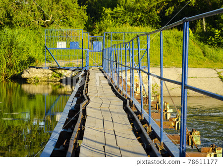 A pedestrian steel bridge with railings and a wooden floor runs through the river dam. 78611177