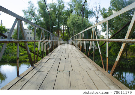 A pedestrian steel bridge with handrails and a wooden floor passes through the river 78611179