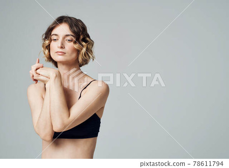 A woman in a short T-shirt on a gray background gestures with her hands to her bare shoulders Fitness Yoga asana 78611794